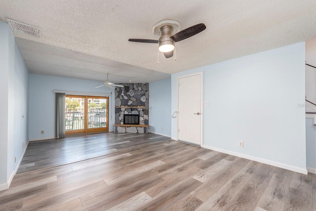 unfurnished living room with ceiling fan, a stone fireplace, a textured ceiling, and light wood-type flooring