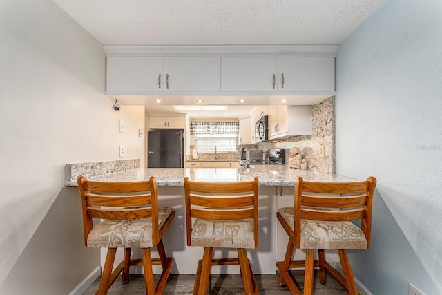 kitchen with sink, white cabinets, a kitchen bar, decorative backsplash, and black fridge