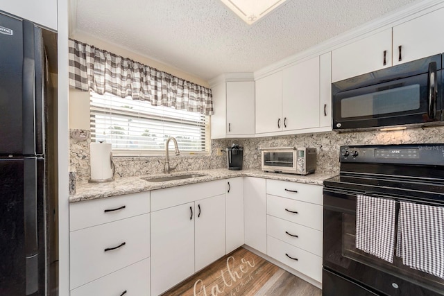 kitchen with black appliances, sink, white cabinets, light stone counters, and light hardwood / wood-style floors