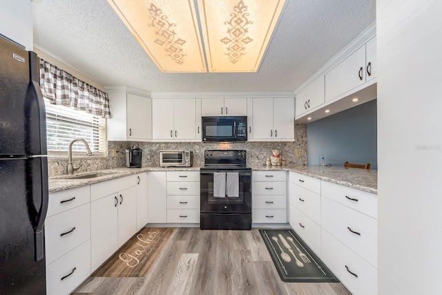 kitchen featuring sink, black appliances, white cabinets, and light stone countertops