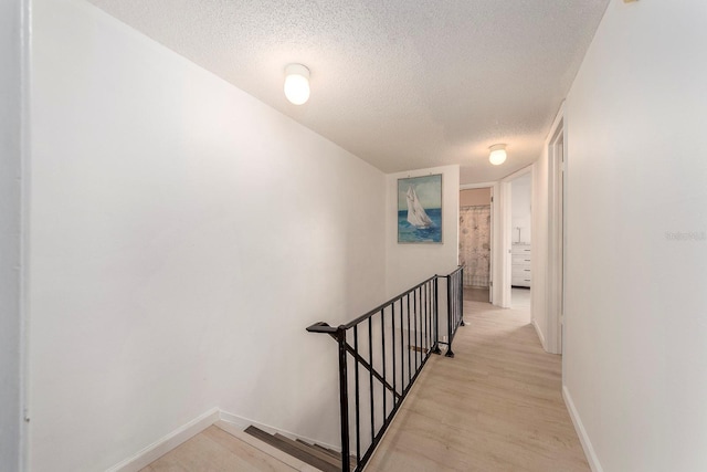 hall featuring light wood-type flooring and a textured ceiling