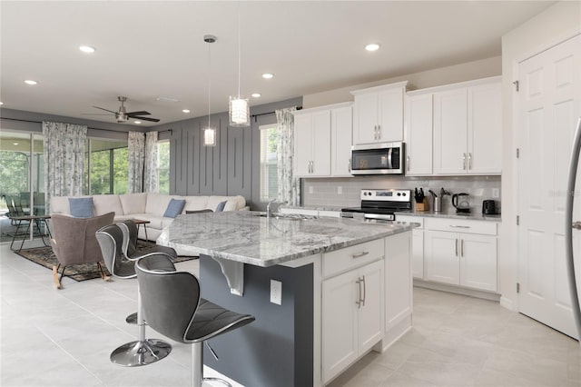 kitchen featuring white cabinetry, appliances with stainless steel finishes, a center island with sink, and decorative light fixtures