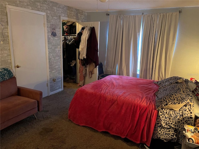 bedroom featuring brick wall, dark carpet, a closet, and a walk in closet