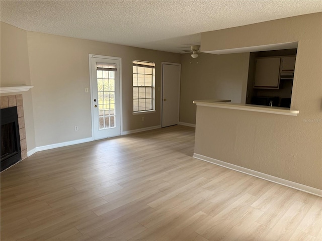 5635 Devonbriar Way Unit 103, Orlando, FL 32822 - unfurnished living room with a textured ceiling, a tiled fireplace, a ceiling fan, and light wood-style flooring
