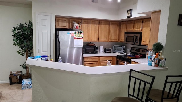 kitchen with appliances with stainless steel finishes, brown cabinets, a breakfast bar, a peninsula, and light countertops