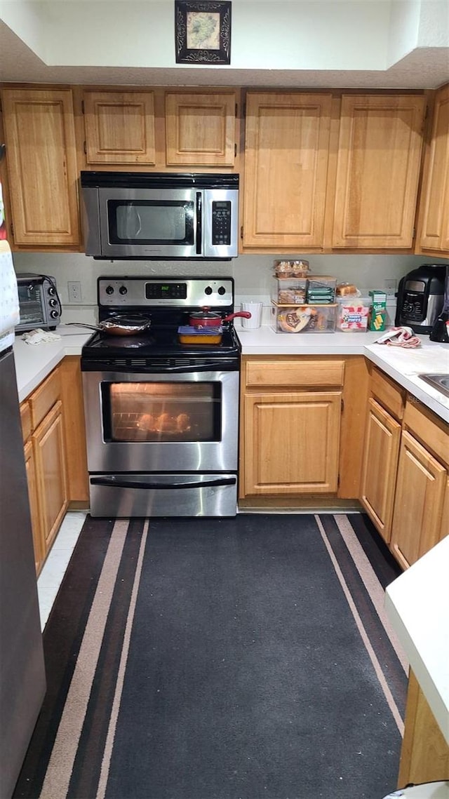 kitchen with light brown cabinets, stainless steel appliances, light countertops, and a toaster