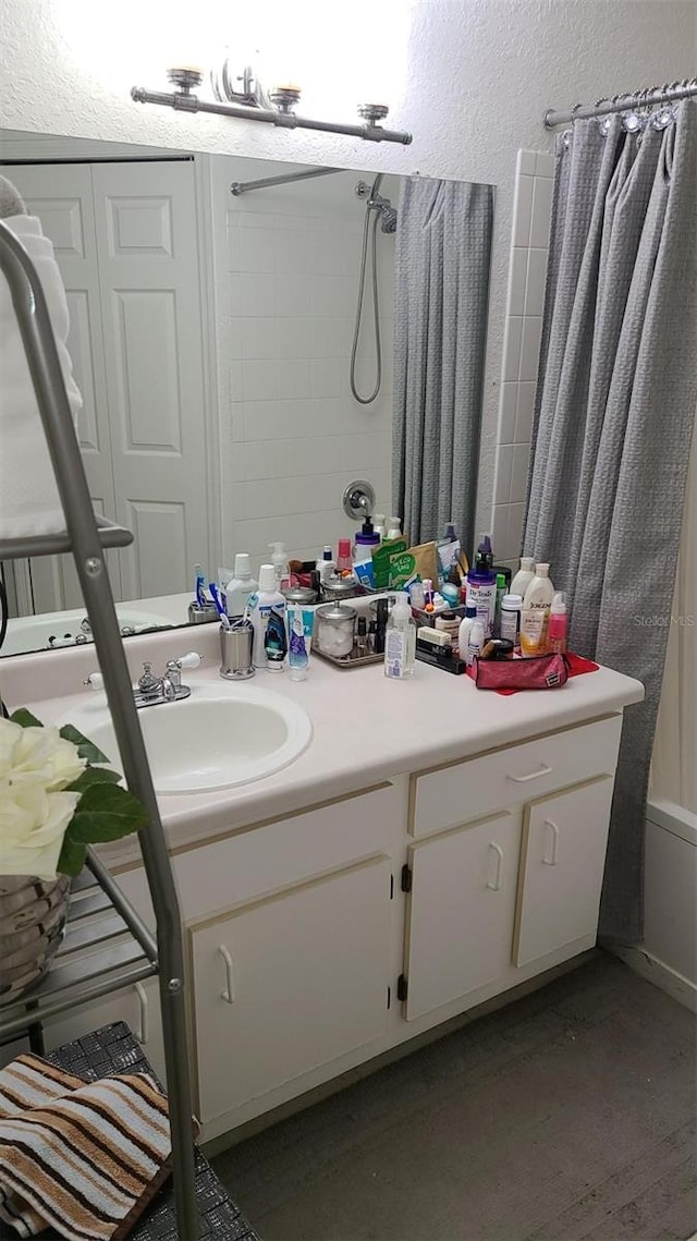 bathroom featuring curtained shower, a textured wall, and vanity