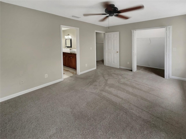 unfurnished bedroom featuring a closet, a walk in closet, ceiling fan, connected bathroom, and light carpet