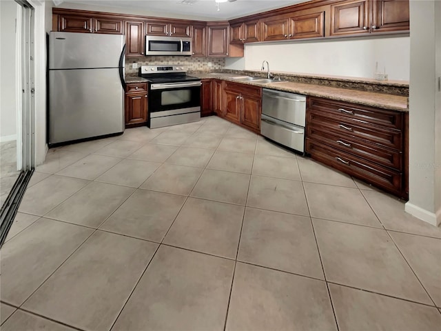 kitchen with appliances with stainless steel finishes, sink, light tile floors, light stone counters, and tasteful backsplash