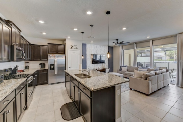 kitchen featuring an island with sink, stainless steel appliances, decorative light fixtures, ceiling fan, and sink