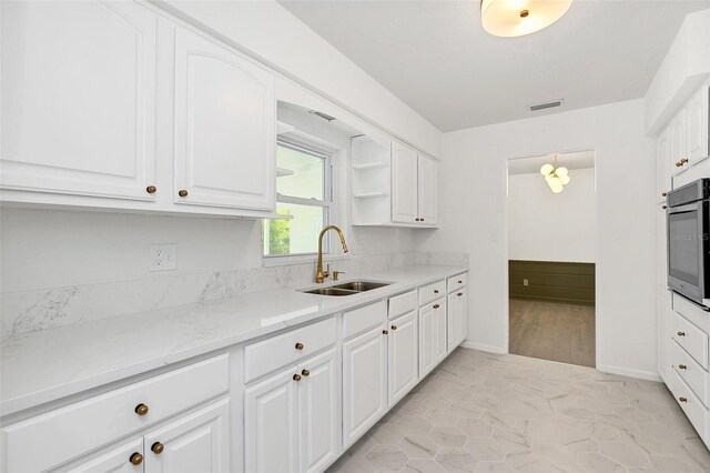 kitchen with oven, sink, light stone counters, light wood-type flooring, and white cabinets