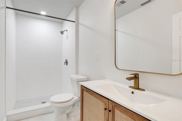 bathroom featuring toilet, a tile shower, and vanity