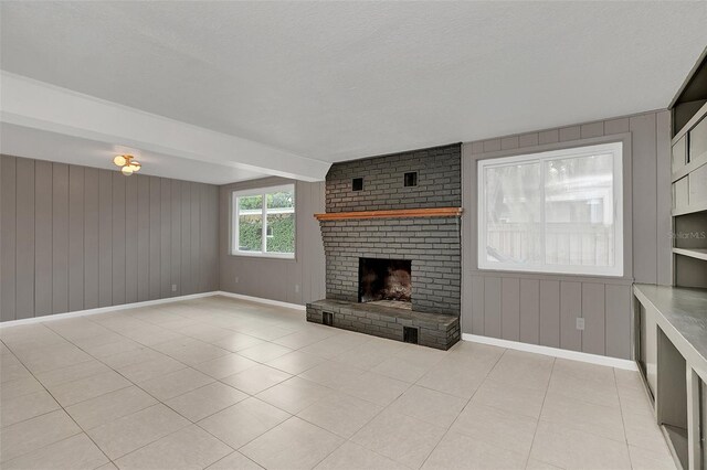 unfurnished living room featuring a textured ceiling, beamed ceiling, a brick fireplace, and light tile patterned floors