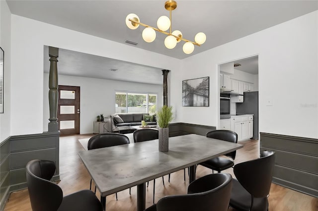 dining area featuring decorative columns, an inviting chandelier, and light hardwood / wood-style flooring