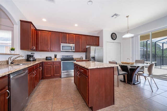 kitchen with hanging light fixtures, appliances with stainless steel finishes, sink, light stone counters, and a kitchen island