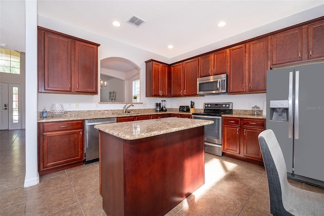 kitchen with light stone countertops, appliances with stainless steel finishes, dark tile floors, a center island, and a chandelier