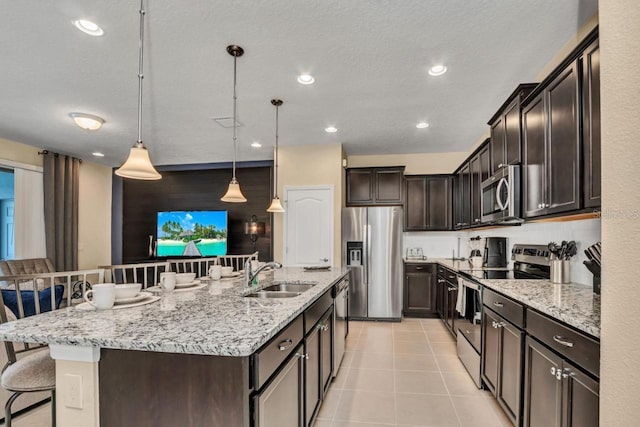 kitchen featuring stainless steel appliances, light tile floors, a kitchen bar, hanging light fixtures, and sink