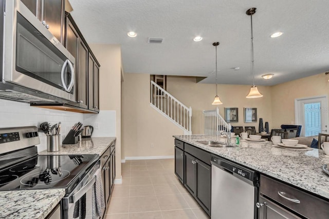 kitchen with pendant lighting, light stone counters, appliances with stainless steel finishes, backsplash, and dark brown cabinetry