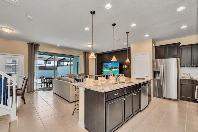 kitchen with decorative light fixtures, a kitchen breakfast bar, appliances with stainless steel finishes, sink, and an island with sink