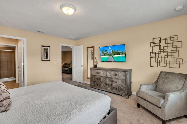 bedroom with a textured ceiling, light colored carpet, and ensuite bathroom