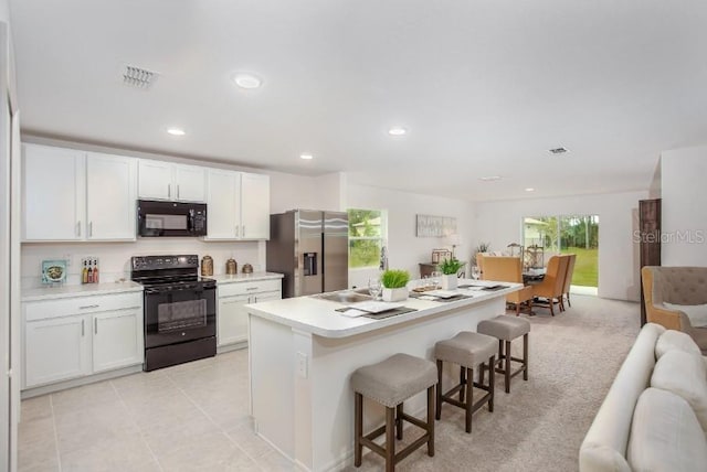 kitchen with a kitchen island with sink, white cabinets, a breakfast bar, and black appliances