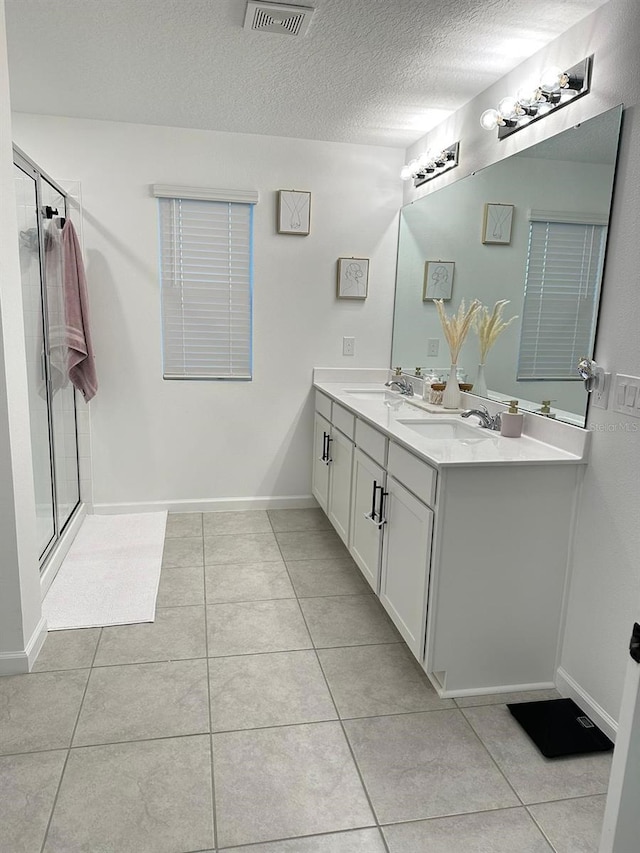 bathroom featuring an enclosed shower, dual vanity, tile flooring, and a textured ceiling