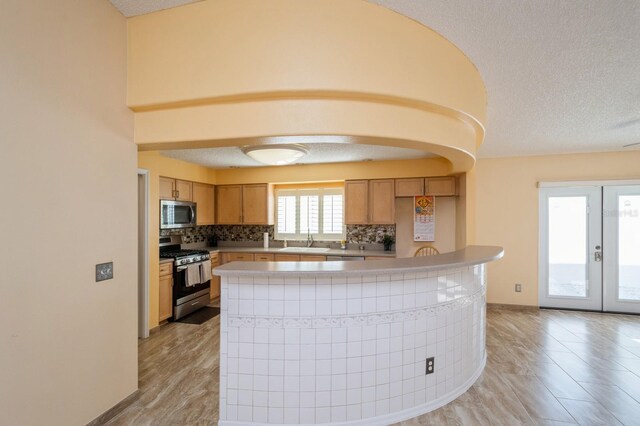 kitchen with a textured ceiling, french doors, tasteful backsplash, appliances with stainless steel finishes, and sink