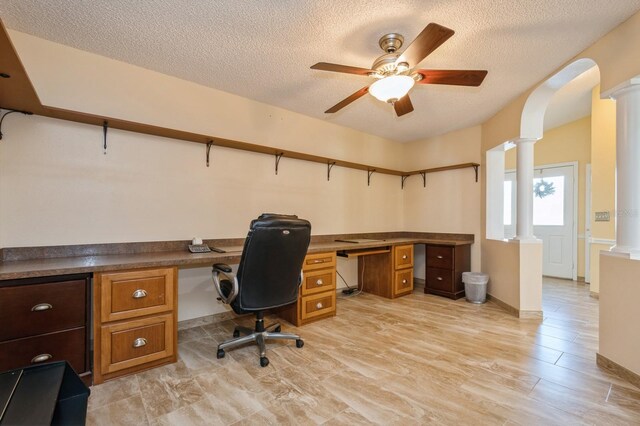 office area featuring a textured ceiling, ornate columns, ceiling fan, and built in desk