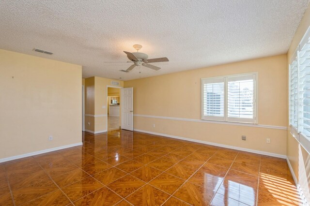 spare room with a textured ceiling, dark tile floors, and ceiling fan