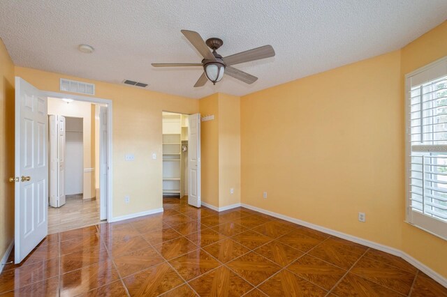 unfurnished bedroom with a walk in closet, dark tile floors, and ceiling fan