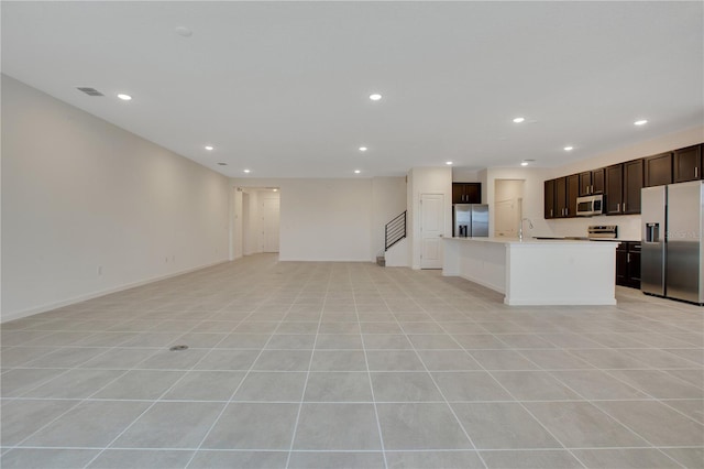 kitchen featuring stainless steel appliances, light tile flooring, a center island with sink, dark brown cabinets, and sink