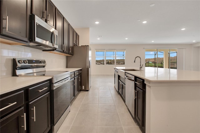 kitchen with an island with sink, light tile floors, appliances with stainless steel finishes, backsplash, and sink