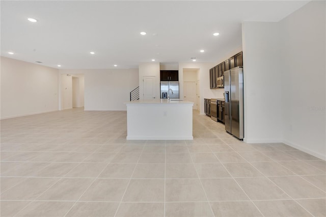 kitchen featuring a center island with sink, stainless steel appliances, light tile floors, and dark brown cabinetry