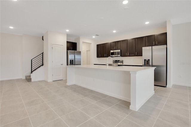 kitchen featuring light tile flooring, a breakfast bar, stainless steel appliances, a center island with sink, and dark brown cabinetry