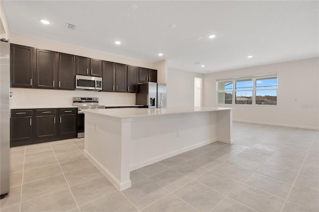 kitchen featuring an island with sink, dark brown cabinetry, light tile floors, and appliances with stainless steel finishes