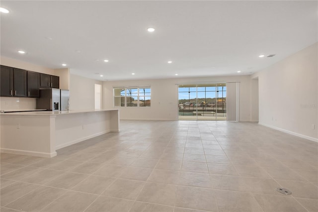 kitchen featuring light tile floors, stainless steel fridge with ice dispenser, dark brown cabinetry, and an island with sink