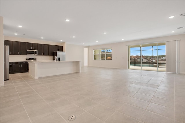 kitchen featuring stainless steel appliances, light tile flooring, a kitchen island with sink, and dark brown cabinetry