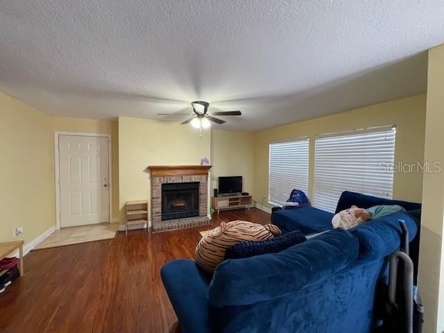 living room with a textured ceiling, a brick fireplace, ceiling fan, and dark hardwood / wood-style floors