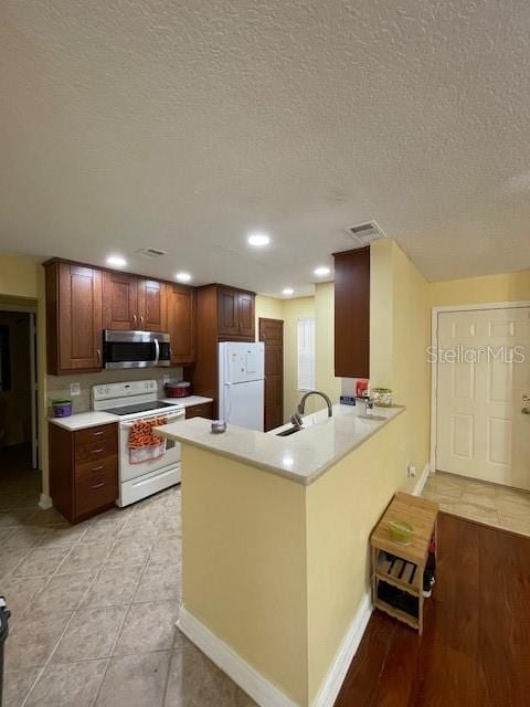 kitchen with kitchen peninsula, white appliances, a textured ceiling, and light tile floors