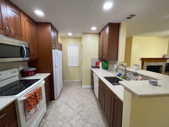 kitchen with a brick fireplace, white appliances, sink, and kitchen peninsula