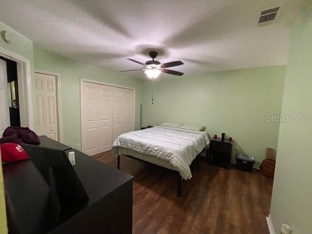 bedroom featuring ceiling fan, a textured ceiling, multiple closets, and dark wood-type flooring