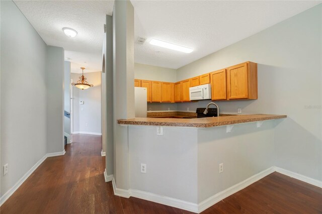 kitchen featuring dark hardwood / wood-style flooring, white appliances, a kitchen bar, and a textured ceiling