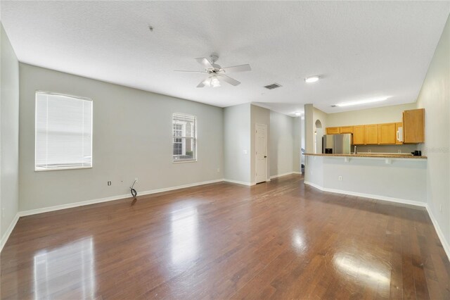 unfurnished living room featuring dark wood-type flooring, a textured ceiling, and ceiling fan