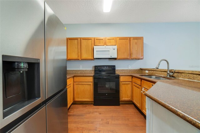 kitchen with light wood-type flooring, sink, stainless steel fridge, black / electric stove, and a textured ceiling