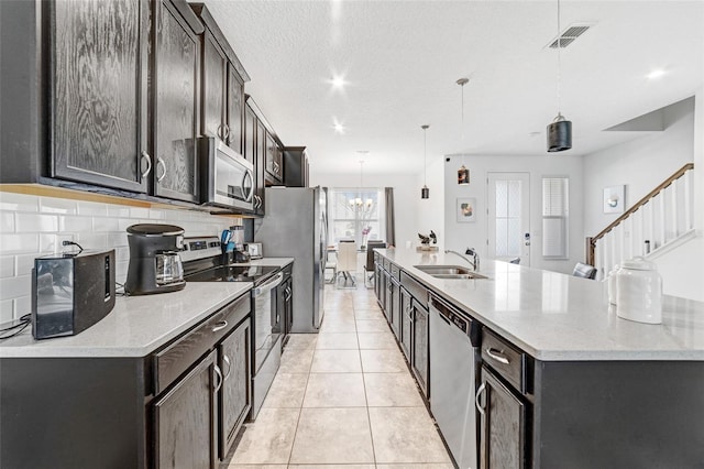 kitchen featuring hanging light fixtures, backsplash, an inviting chandelier, appliances with stainless steel finishes, and a center island with sink