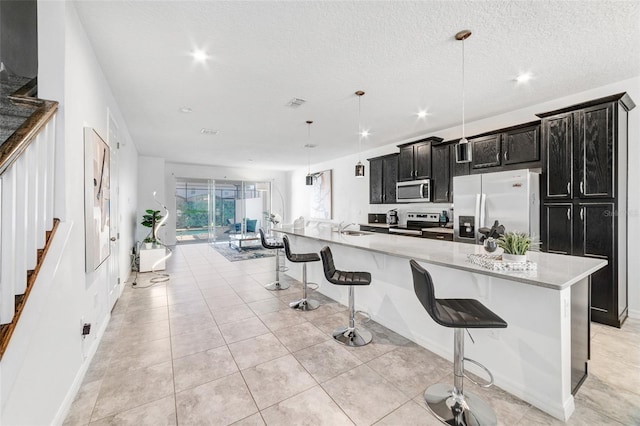 kitchen with an island with sink, decorative light fixtures, appliances with stainless steel finishes, and light stone countertops