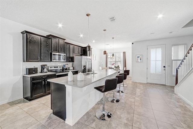 kitchen with stainless steel appliances, light tile floors, a kitchen bar, a center island with sink, and hanging light fixtures