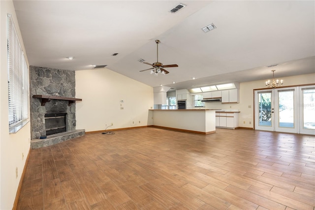 unfurnished living room featuring light hardwood / wood-style floors, vaulted ceiling, a stone fireplace, and ceiling fan with notable chandelier