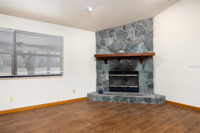 unfurnished living room with a stone fireplace and dark wood-type flooring