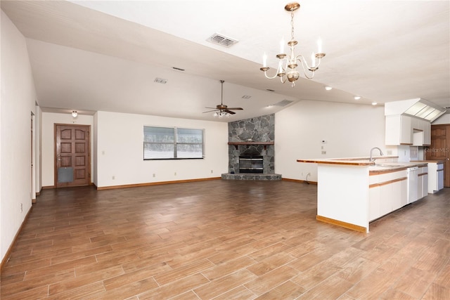 unfurnished living room with sink, light hardwood / wood-style flooring, a fireplace, ceiling fan with notable chandelier, and lofted ceiling